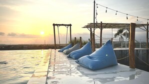 Zona de piscina con sillones colgantes azules, un pérgola y vistas al atardecer.