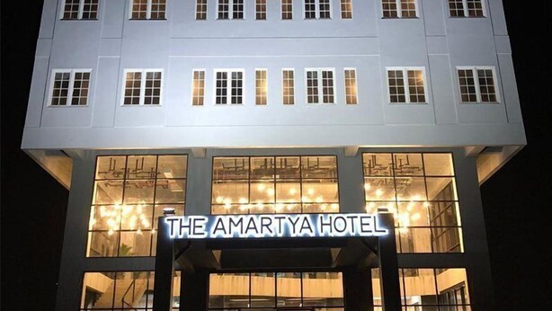 Hotel Amartya con una fachada moderna, amplias ventanas y un llamativo letrero iluminado.