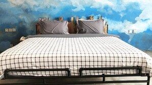 Una cama con colcha a cuadros, cabecera de madera y pared decorada con un mural de nubes.