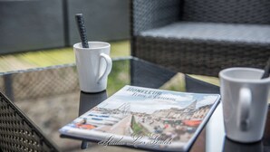Une table en verre sur laquelle se trouvent une tasse blanche, une brochure intitulée « Honneur Terre d’Estuaire » et une tasse noir et blanc.