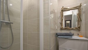 Une salle de bain dotée d’une douche à parois de verre, d’un miroir à cadre en bois et d’un meuble-lavabo blanc, avec une serviette et des articles de toilette.