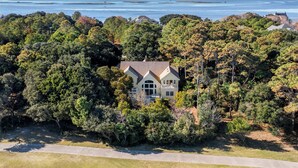 Une grande maison entourée d’une forêt dense, avec une vue sur l’océan en arrière-plan.