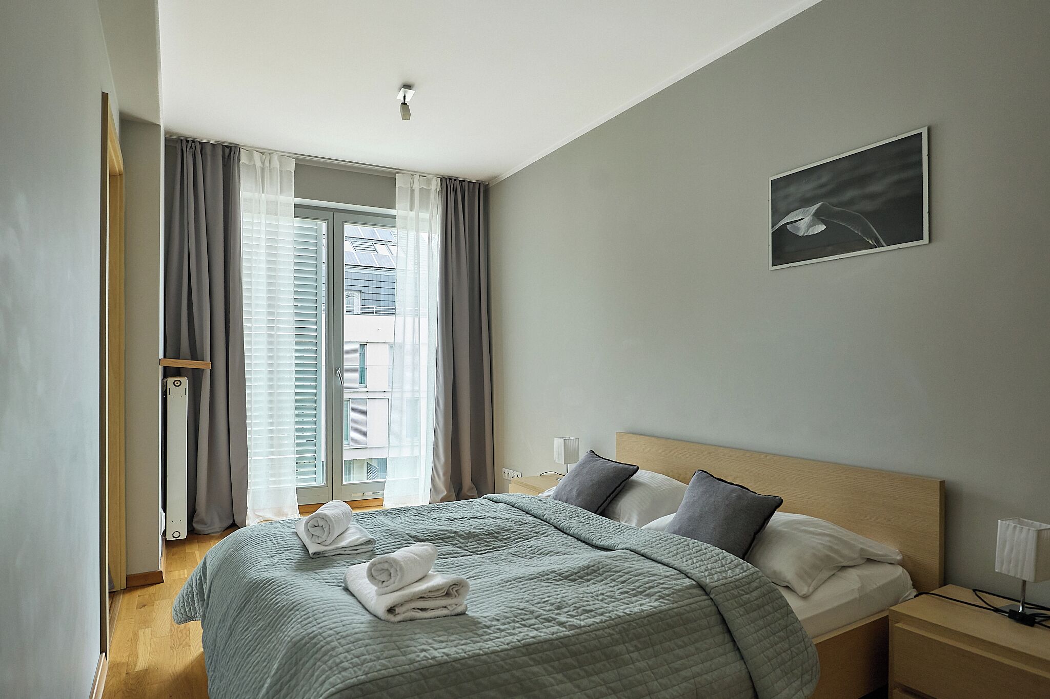 Une chambre d’hôtel comprenant un lit, une table de chevet, une commode, une fenêtre avec des rideaux et un tableau accroché au mur.