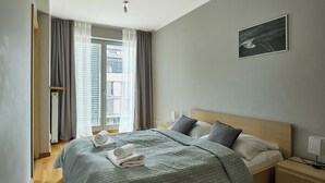 A hotel room with a bed, a bedside table, a nightstand, a window with curtains, and a wall-mounted picture. - Apartamenty Swinoujscie - Casa Marina (Swinoujscie)