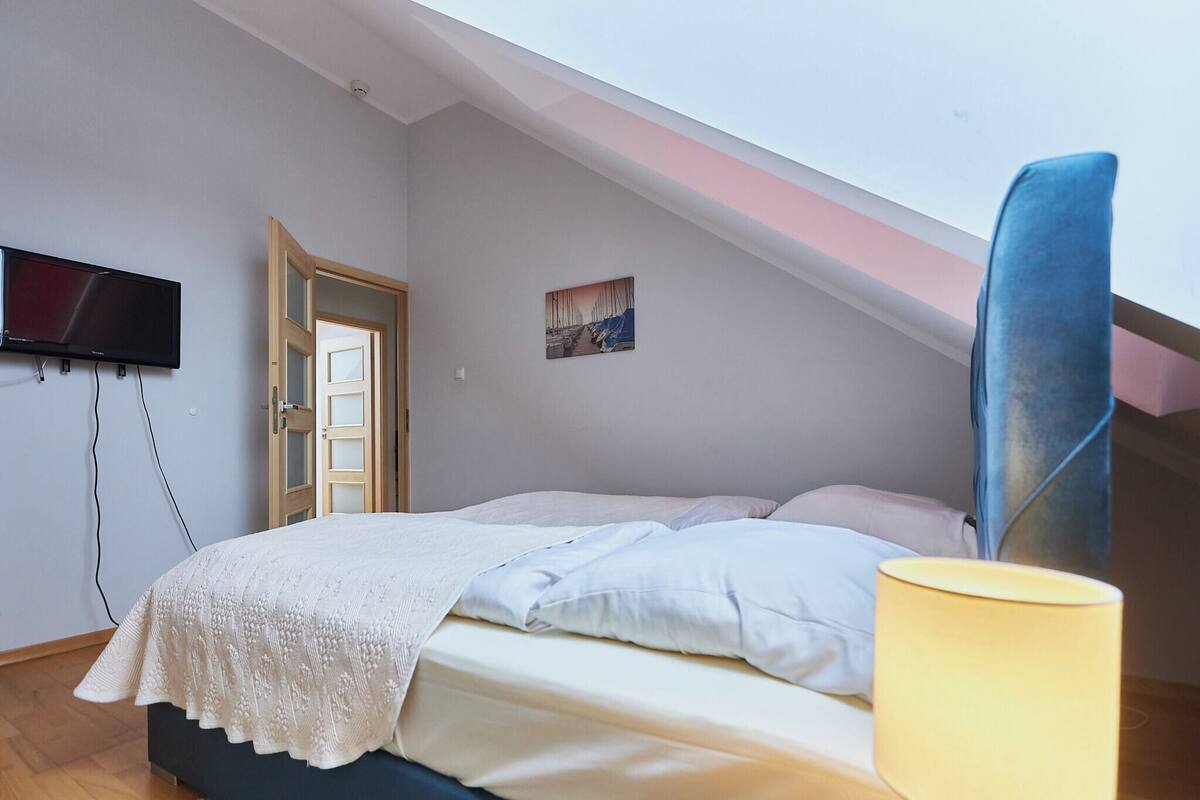 Een slaapkamer met een bed, een aan de muur bevestigde televisie, een deur en een schilderij.
