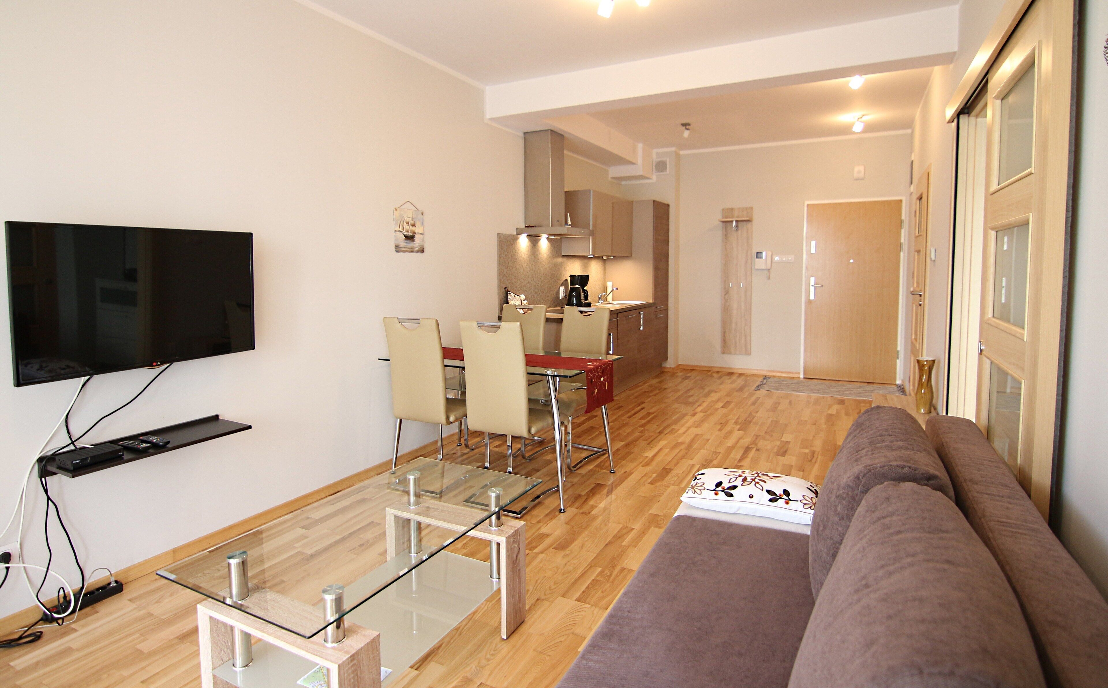 A modern living room with a flat-screen TV, glass-top coffee table, and a sofa.