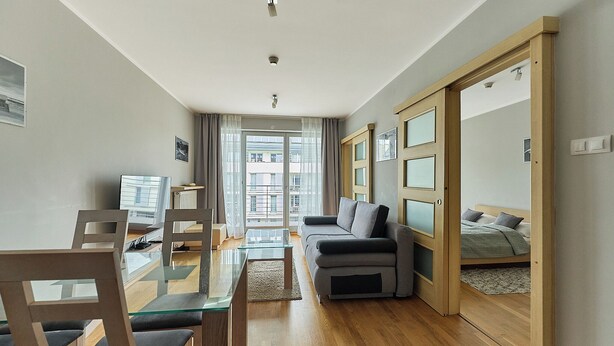 A modern living room with a sofa, a glass coffee table, and a dining area with chairs. - Apartamenty Swinoujscie - Casa Marina (Swinoujscie)
