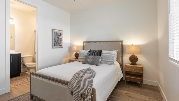A bedroom with a bed, bedside tables, a nightstand, a bedside lamp, a wall-mounted picture, and a door leading to a bathroom. - Desert Azul: Desert Color Lagoon + Beaches (St, George)