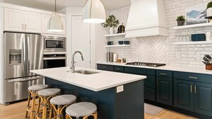 Cocina moderna con armarios blancos, refrigerador de acero inoxidable, microondas, pileta y una barra con taburetes.