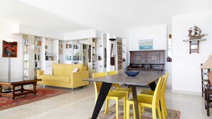 A living room with a yellow sofa, a dining table with yellow chairs, and a bookshelf filled with books. - On la Croisette XXL 1 bedroom with amazing sea view (Cannes)