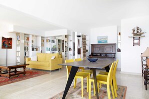 A living room with a yellow sofa, a dining table with yellow chairs, and a bookshelf filled with books.
