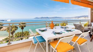 A balcony with a table set for dining, overlooking a coastal view with boats and palm trees. - On la Croisette XXL 1 bedroom with amazing sea view (Cannes)