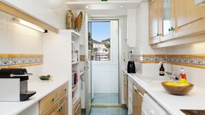 A narrow kitchen with white cabinets, a coffee machine, a sink, and a view through an open door. - On la Croisette XXL 1 bedroom with amazing sea view (Cannes)