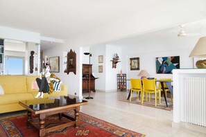 A living room with a yellow sofa, a coffee table, a dining area with yellow chairs, and a white radiator.