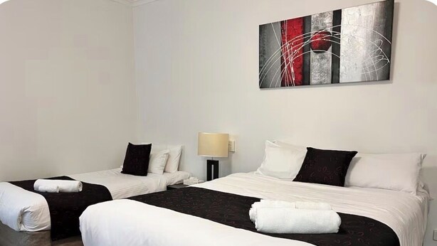 A hotel room with two beds, a nightstand, a lamp, and a painting on the wall.