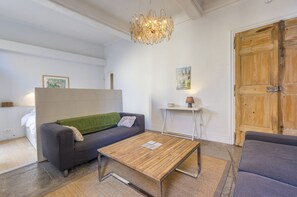 A modern living room with a grey sofa, a wooden coffee table, a chandelier, and a wooden door.