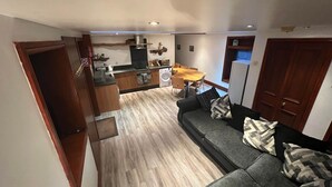 A compact living space with a kitchenette, a dining area, and a sofa with cushions. - Ochiltree Cottage, Waterside Newton Stewart. (Polbae)