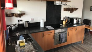 A modern kitchen with wooden cabinets, a black countertop, a stainless steel kettle, a coffee maker, and a microwave. - Ochiltree Cottage, Waterside Newton Stewart. (Polbae)