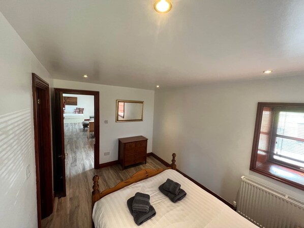 A bedroom with a wooden bed, a dresser, a mirror, and a radiator. - Maberry Cottage, Waterside Newton Stewart. (Polbae)