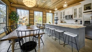 A modern kitchen with white cabinets, a central island with bar stools, and a dining area with a wooden table and chairs.