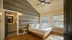 A bedroom with a wooden ceiling, a bed, a small round table, and a window.