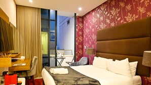A hotel room with a large bed, a desk with a chair, a small table, and a view of the outside. - Trendy Studio Apartment Centrally Located (Johannesburg)