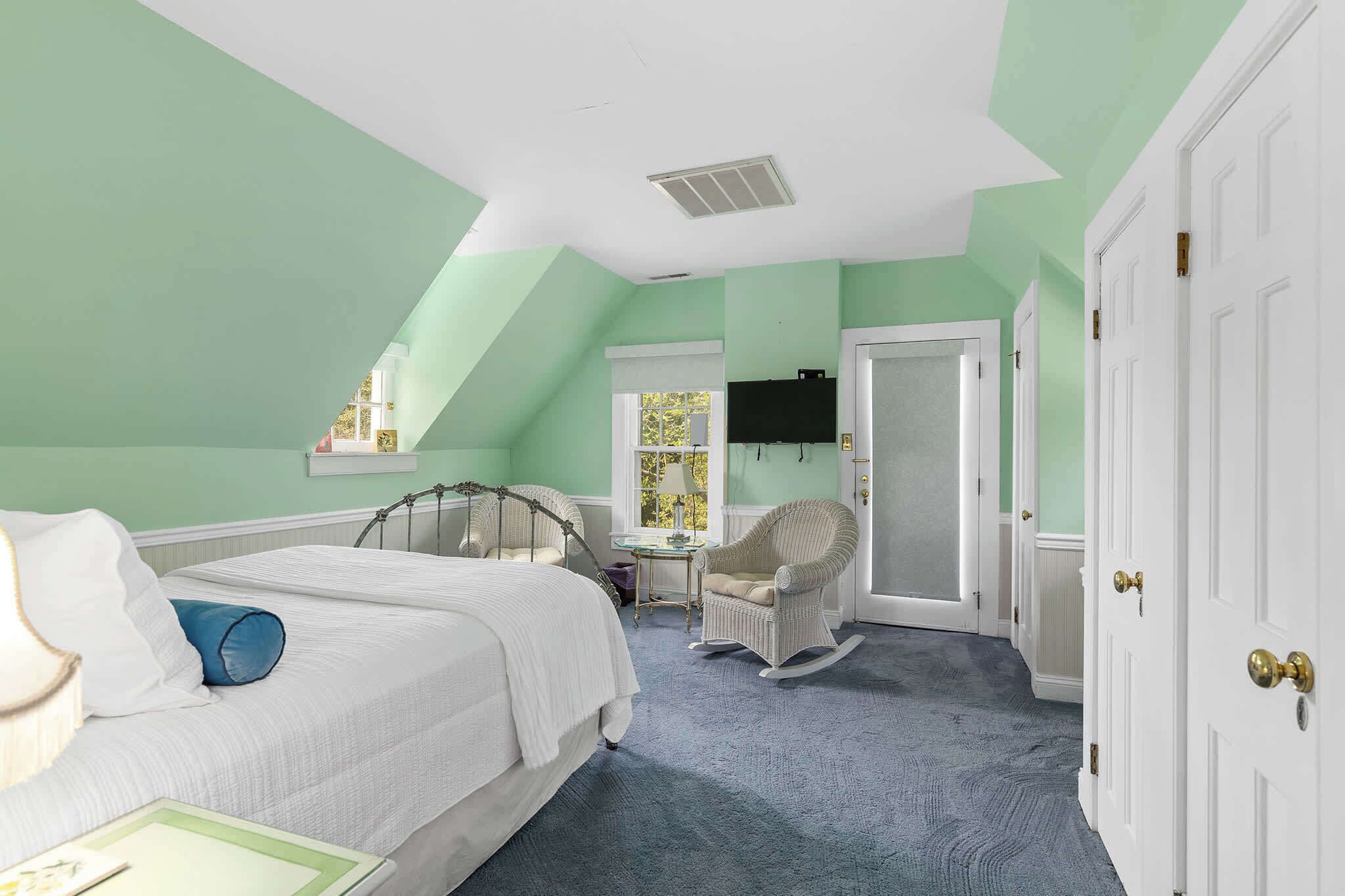 Un dormitorio con cama, sillón mecedora, escritorio y puerta.