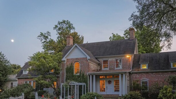 A brick house with a front porch, a small garden, and a white picket fence.