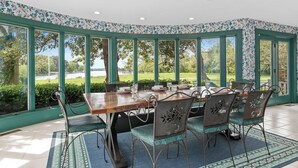 A conservatory with a dining table and chairs, large windows, and a view of the outdoors.