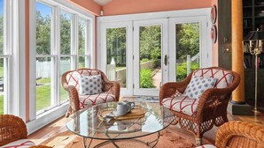 A cozy room with wicker furniture, a glass table, and a view of a garden through large windows.