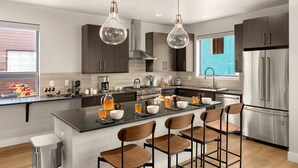 Une cuisine moderne avec des meubles de couleur sombre, des appareils en acier inoxydable et un îlot central doté de tabourets de bar.