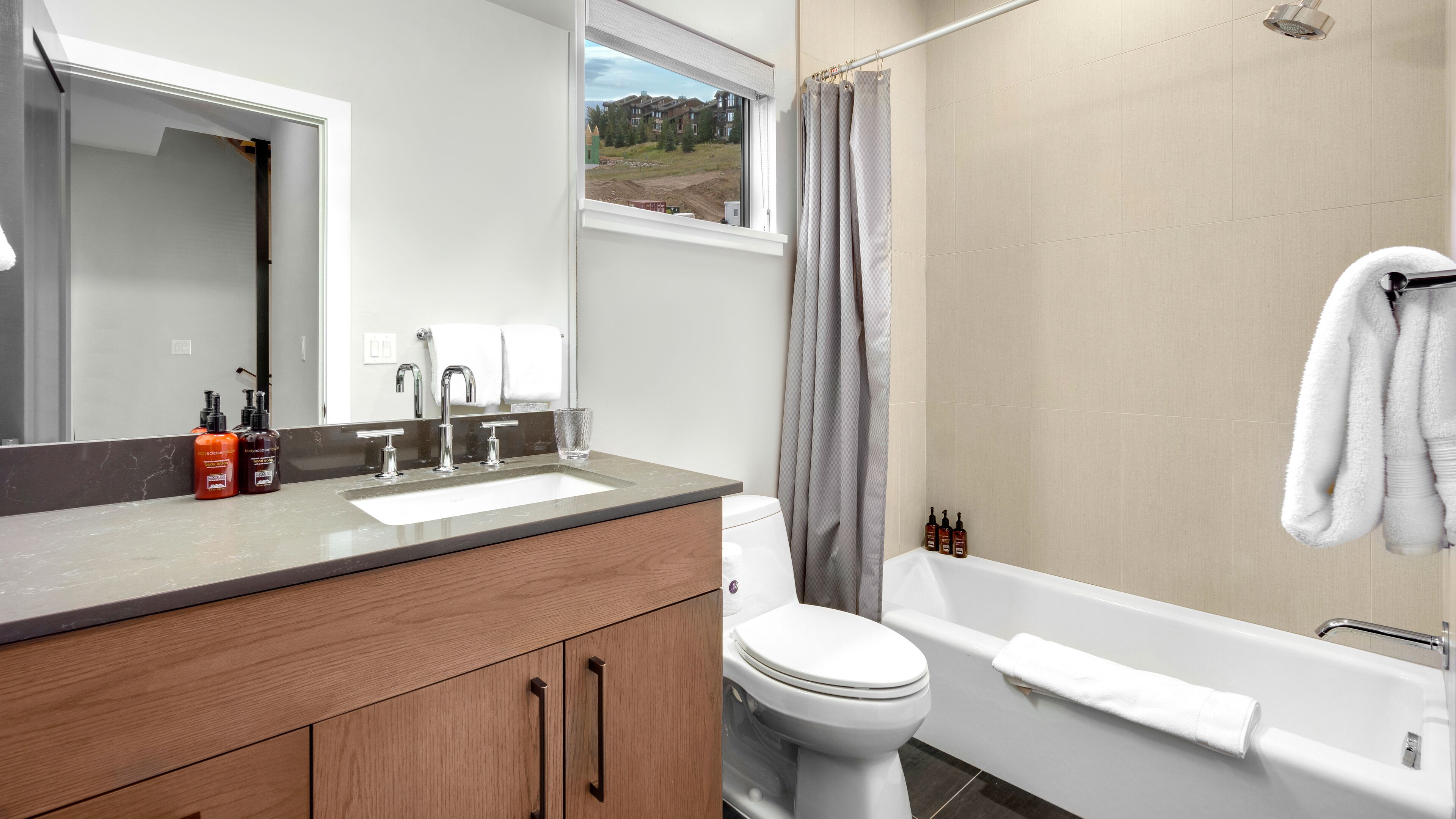 A modern bathroom with a wooden vanity, a large mirror, a toilet, a bathtub, and a shower curtain.