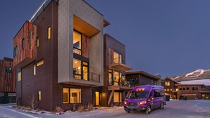 Un immeuble moderne à plusieurs étages, doté de grandes fenêtres, avec un camion de déménagement violet garé devant.