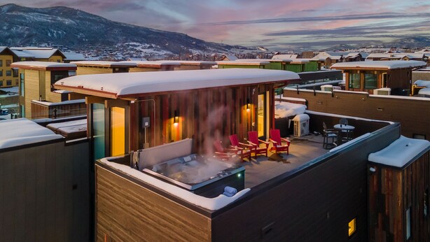 Une terrasse sur le toit avec un jacuzzi, des chaises rouges et une vue sur un village enneigé.