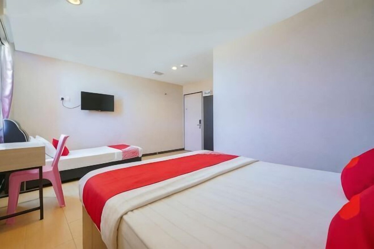 Quarto de hotel com cama, escrivaninha, cadeira, televisão e porta.