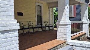 A porch with a wooden deck, white brick columns, and a yellow house exterior. - Charming 4BR Historic Home near Downtown & Duke, Spacious & Stylish (Durham)