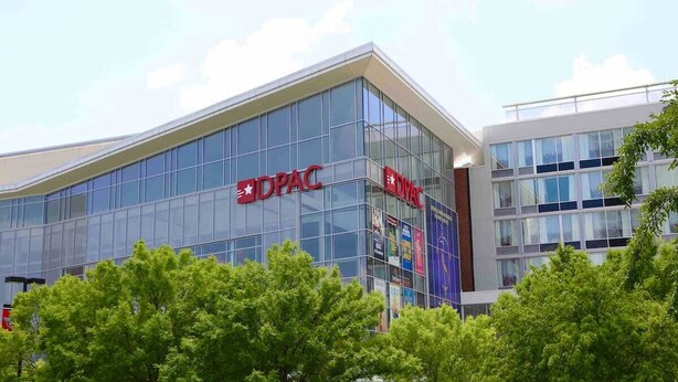 A modern building with the DPAC logo, featuring large glass windows and a prominent entrance. - Charming 4BR Historic Home near Downtown & Duke, Spacious & Stylish (Durham)