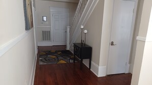 A hallway with wooden flooring, a black console table, a white door, and a staircase with white railings. - Charming 4BR Historic Home near Downtown & Duke, Spacious & Stylish (Durham)