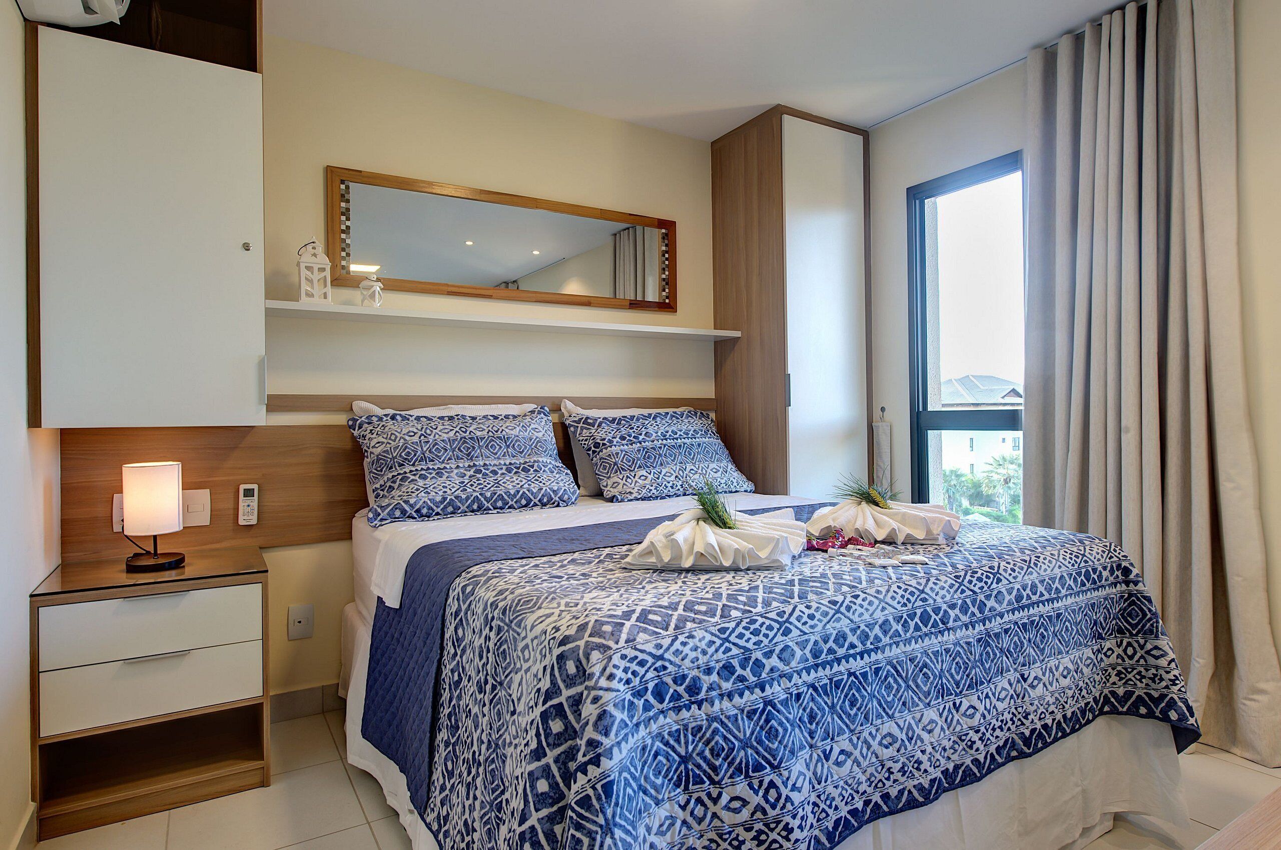 A hotel room with a bed, a nightstand, a mirror, and a window with curtains.