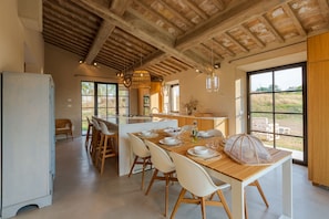 A spacious kitchen with a large island, wooden ceiling beams, and large windows offering views of the outdoors.
