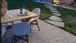 Eine Terrasse im Freien mit einer Steinwand, einem Holztisch mit Gläsern und einer Flasche sowie Lichterketten.
