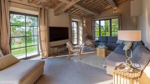 Ein geräumiges Wohnzimmer mit großem Fenster, einer Couch, zwei Sesseln und einem Fernseher.