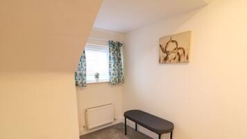 A small, carpeted room with a bench, a radiator, and a window with patterned curtains.