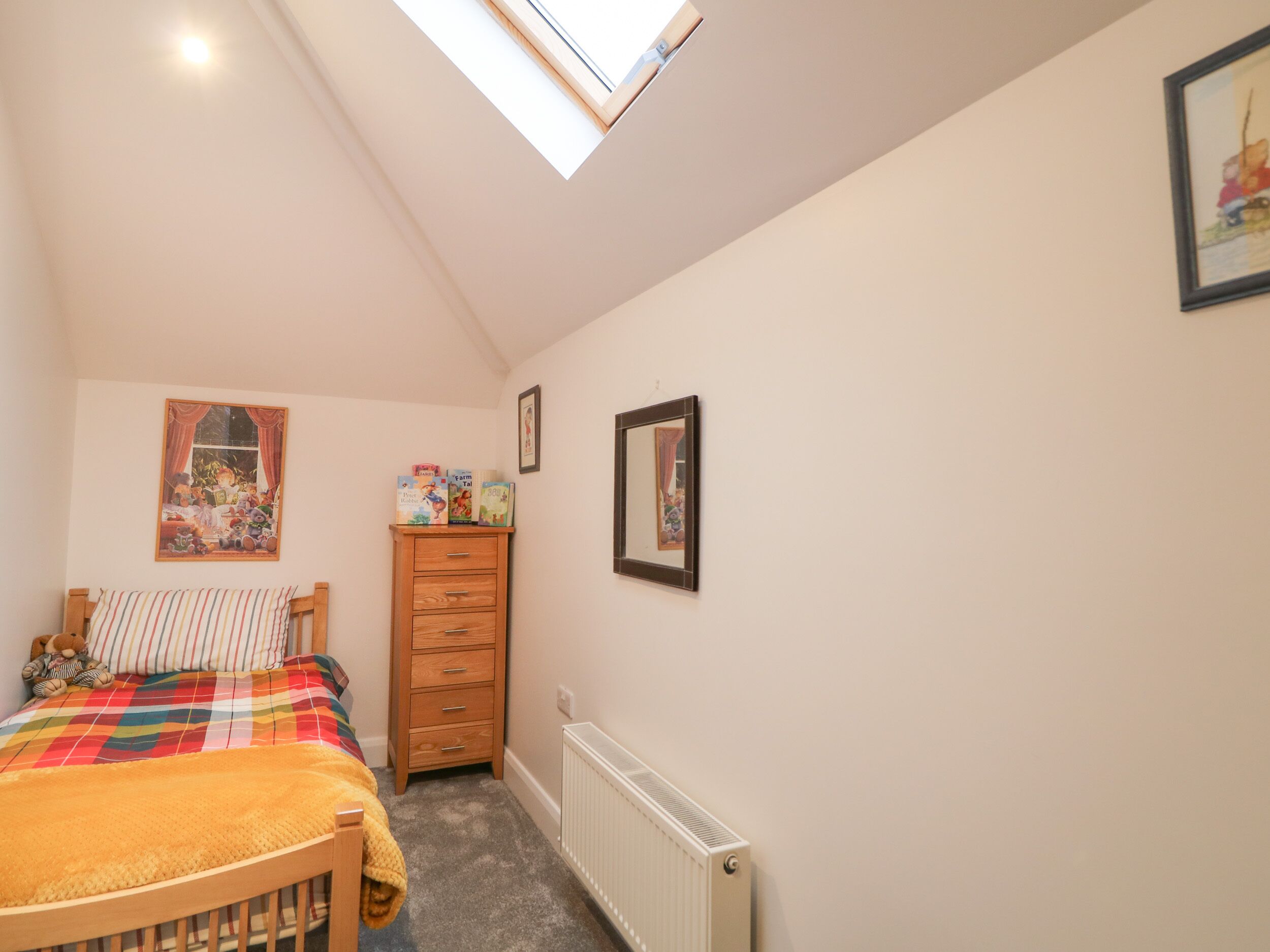 Un dormitorio con cama, cómoda, radiador y tragaluz.