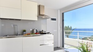 Una cocina moderna con armarios blancos, un lavamanos de acero inoxidable y vista al océano a través de un ventanal.