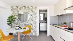 Una cocina moderna con armarios blancos, una campana extractora de acero inoxidable y un comedor con mesa de vidrio y sillas amarillas.