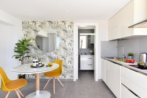 Una cocina moderna con armarios blancos, una campana extractora de acero inoxidable y un comedor con mesa de vidrio y sillas amarillas.