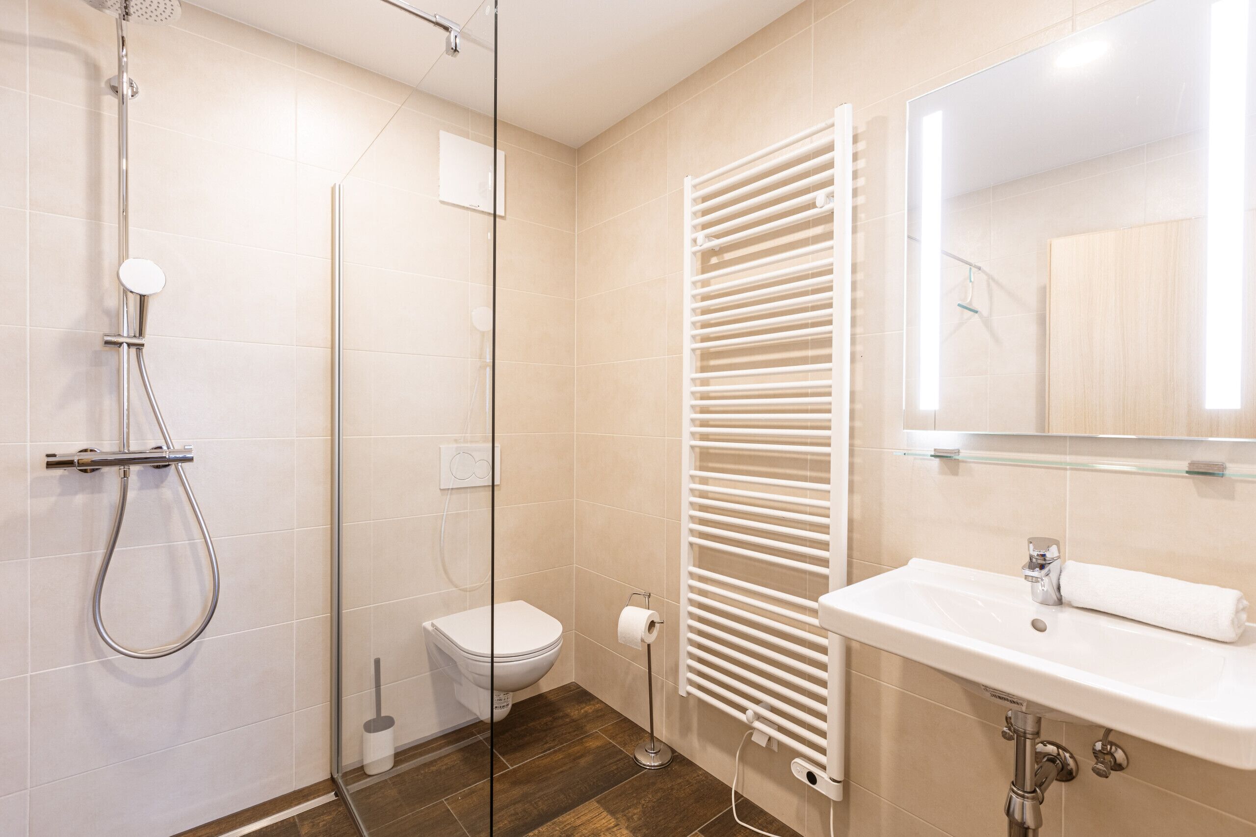 Un baño moderno con cabina de ducha de vidrio, inodoro blanco, barra para toallas y lavabo con espejo superior.