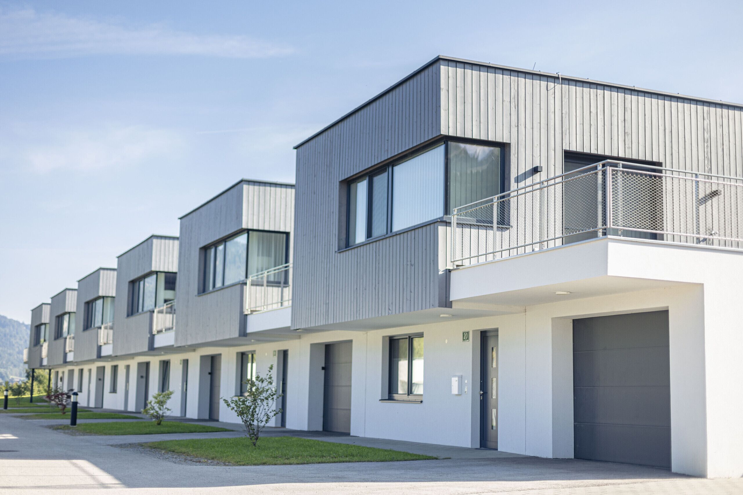 Ein modernes Mehrfamilienhaus mit Flachdach, großen Fenstern und einem Balkon im oberen Geschoss.