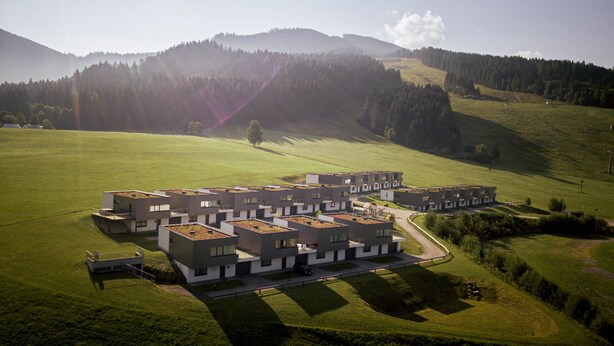 Un complexe résidentiel moderne composé de plusieurs bâtiments, dotés de toits plats et entouré d’un espace vert.